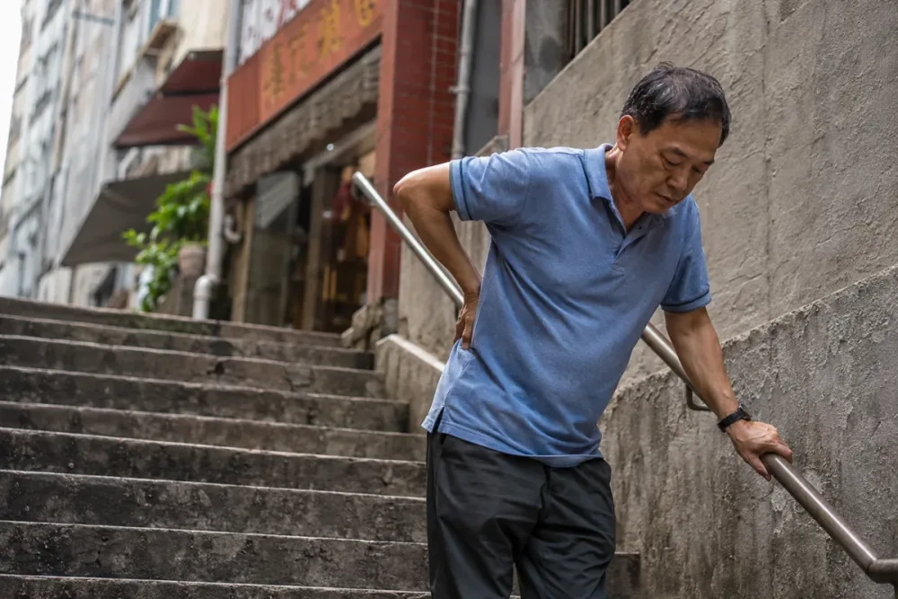 五十幾歲男士喺香港街道樓梯停低,一隻手揤住腰