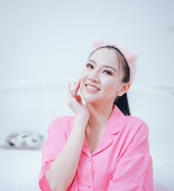 Perempuan berpiyama merah muda menyentuh pipinya di pagi hari