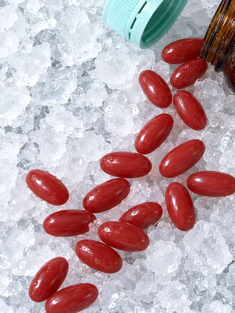 Red HOMEGA softgels spilled from an open bottle across crushed ice.