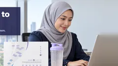 A woman in a tudung smiling at her laptop at the office, her shaker and the Kuro Daitto box on the desk, the Kuala Lumpur towers behind. Full for up to 4 hours. Results vary from person to person.