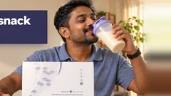 A man drinking a vanilla Kuro Daitto shake and pushing away a plate of curry puffs and crackers, the Kuro Daitto box on the table. Stops the snack cravings.