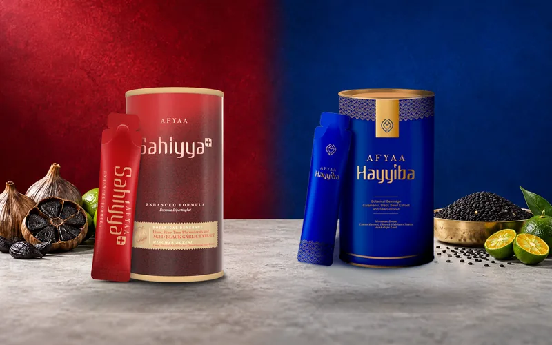 The AFYAA Sahiyya+ tin and sachet on a crimson set with aged black garlic and lime, beside the AFYAA Hayyiba tin and sachet on a royal blue set with habbatus sauda and calamansi.